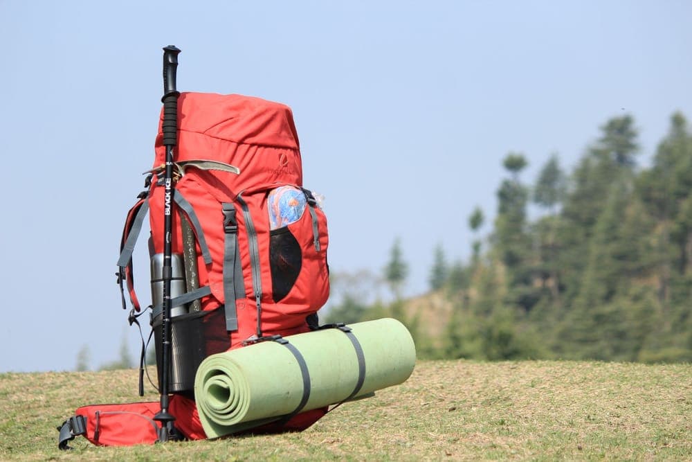 A red backpack with a sleeping mat standing on a grassy hill