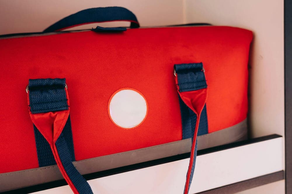 A red duffel bag with blue straps on a shelf