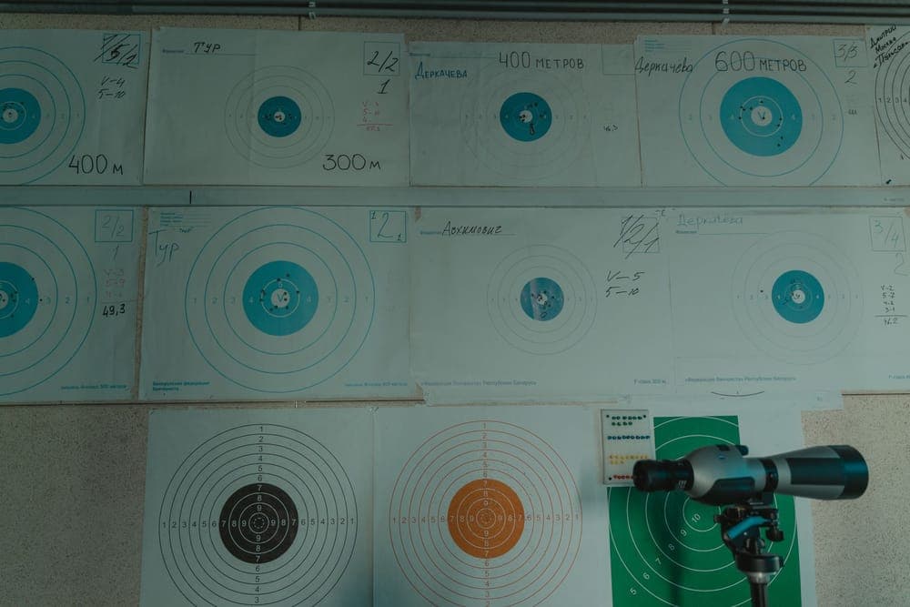 Paper bullseye targets pinned to a wall behind a spotting scope