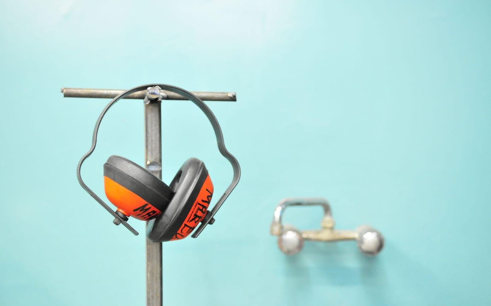 Orange earmuffs hanging on a metal stand against a teal wall