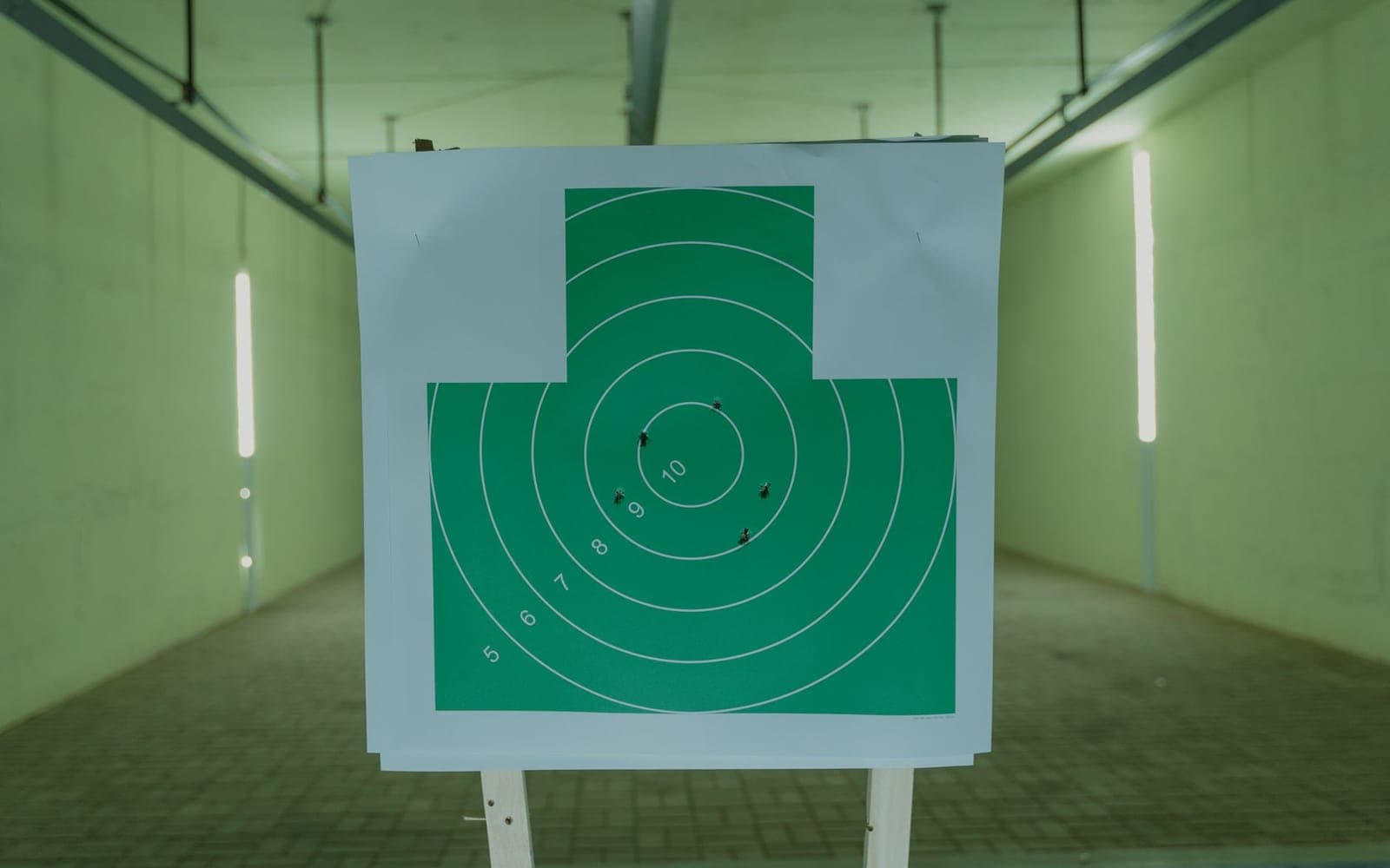A green paper target with bullet holes hanging at an indoor range